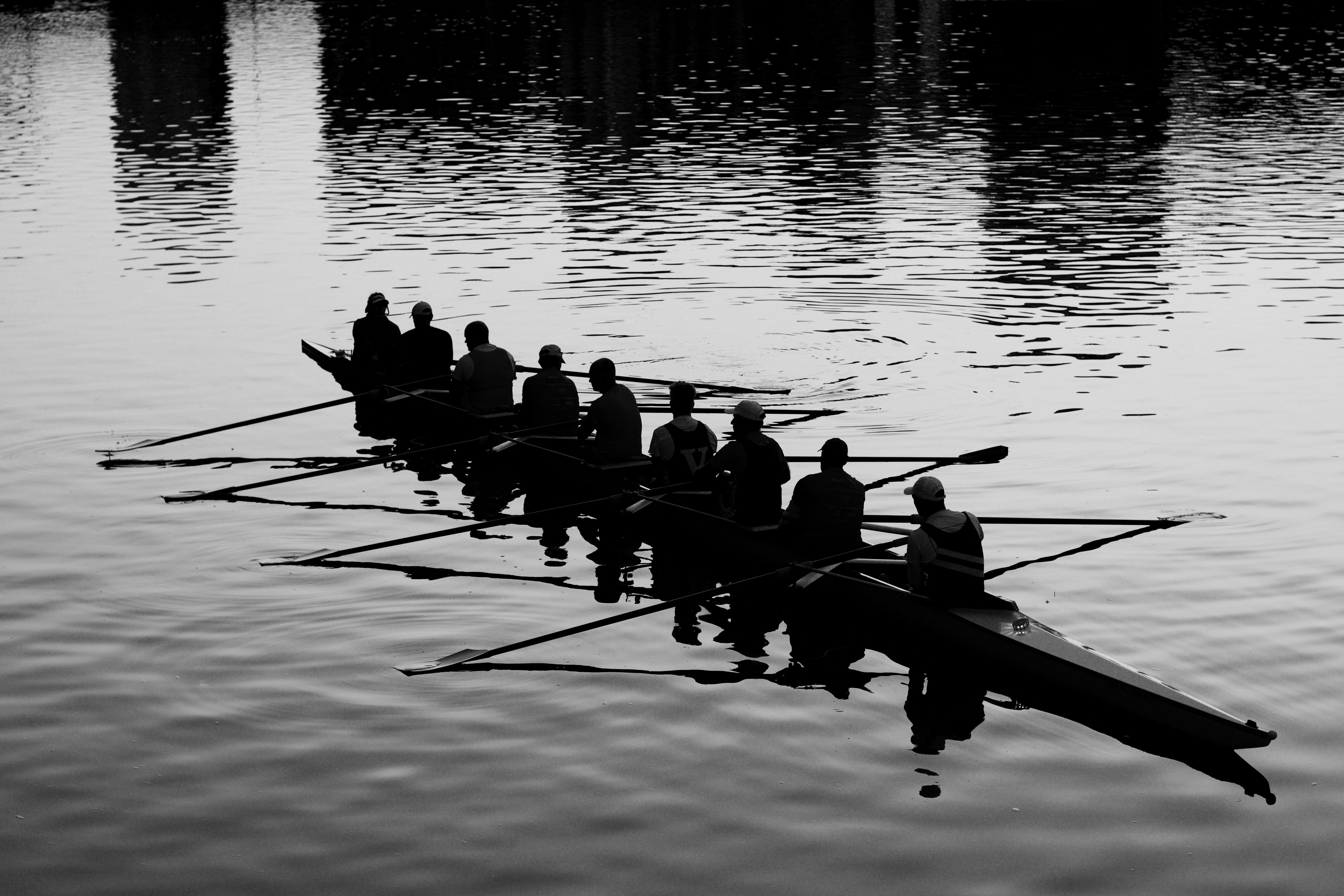 A rowing crew is silhouetted while resting in a shell boat on a calm body of water