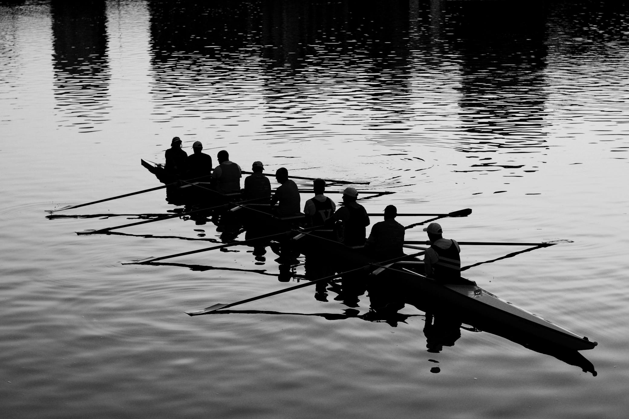 A rowing crew is silhouetted while resting in a shell boat on a calm body of water