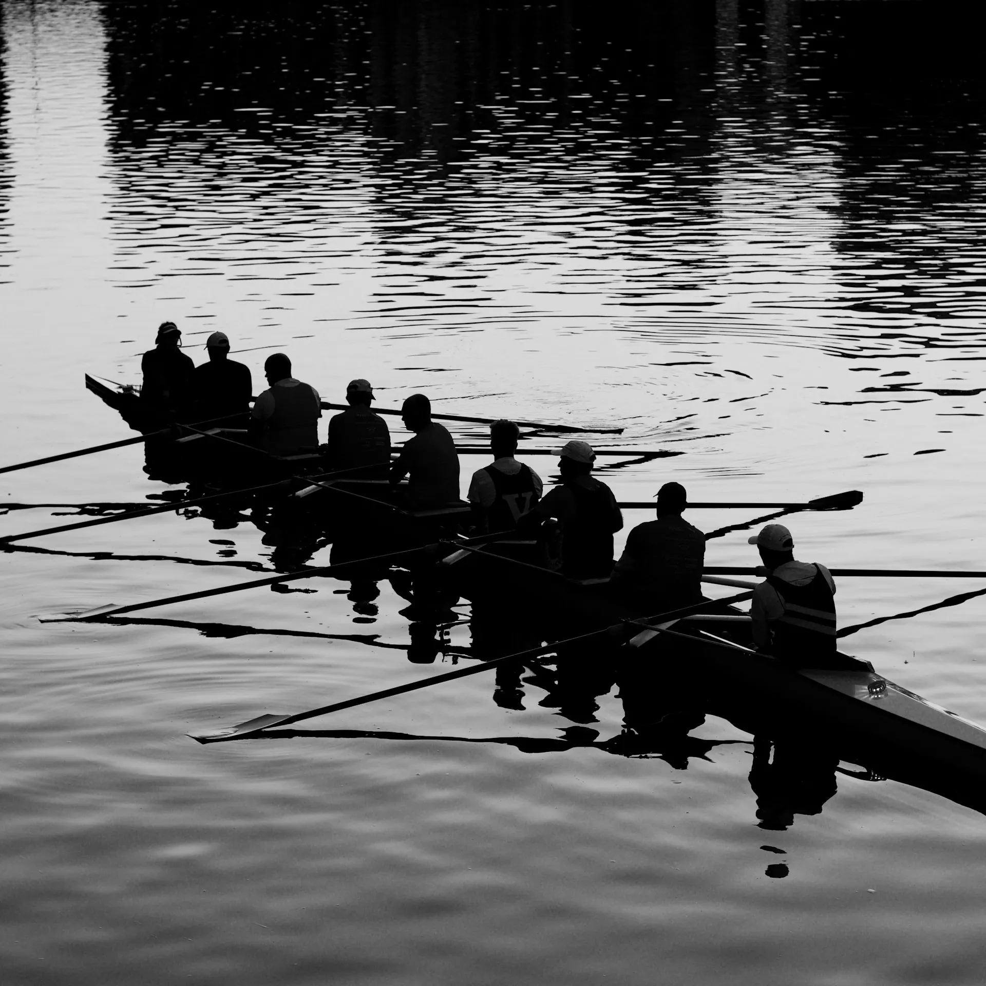 A rowing crew is silhouetted while resting in a shell boat on a calm body of water