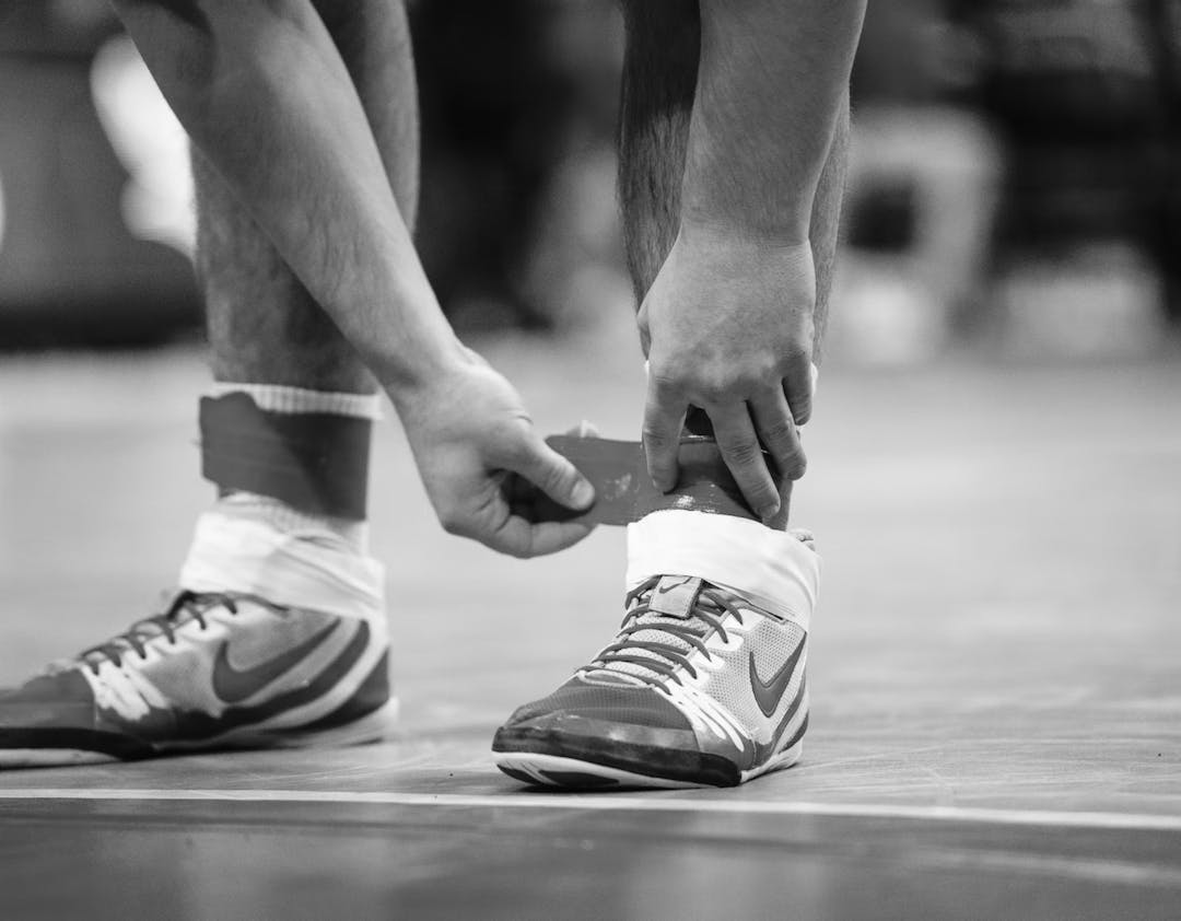 An athlete bends over to tape both ankles before a match