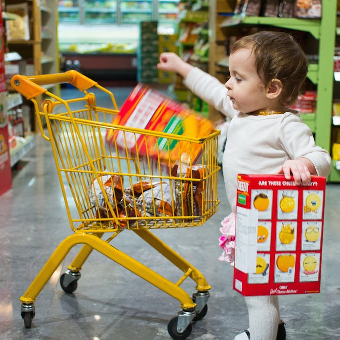 Toddler girl putting cheese-its into a child's size shopping cart