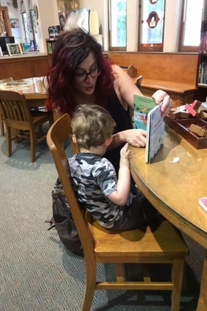 Danielle sitting at a table reading with her two year old son, Luke.
