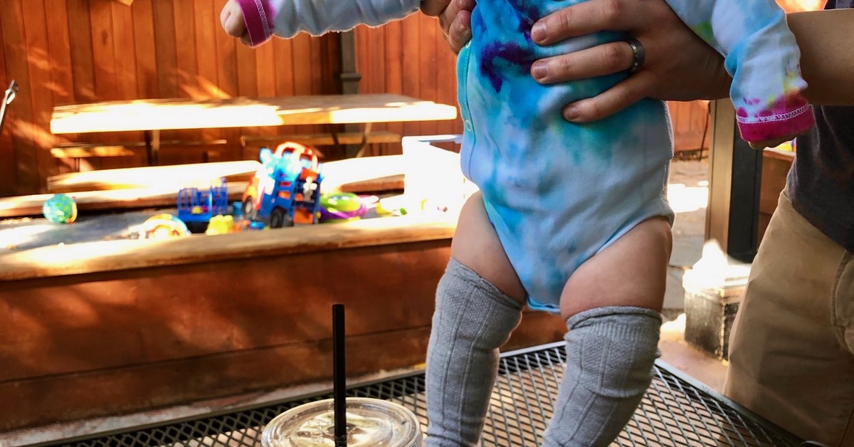 Baby standing on OAM table next to sandwich and tea