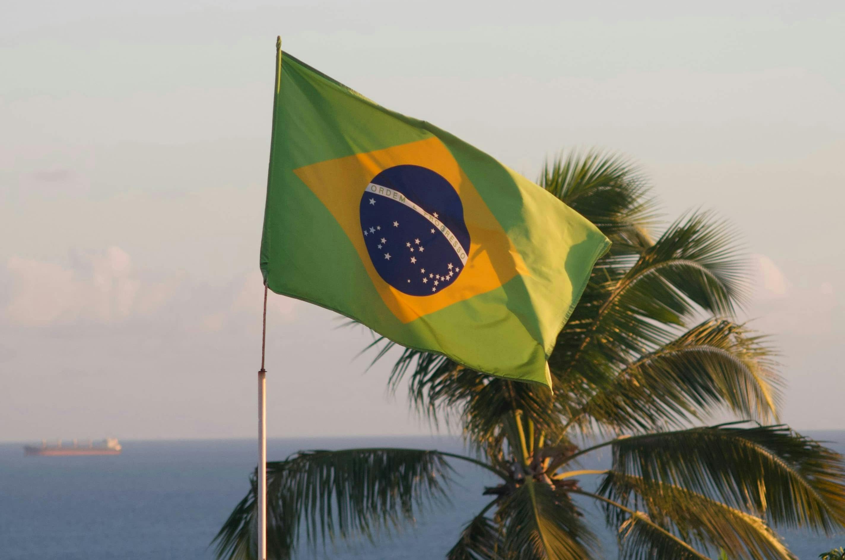 Brazilian flag waving in the wind, with the Atlantic Ocean in the background