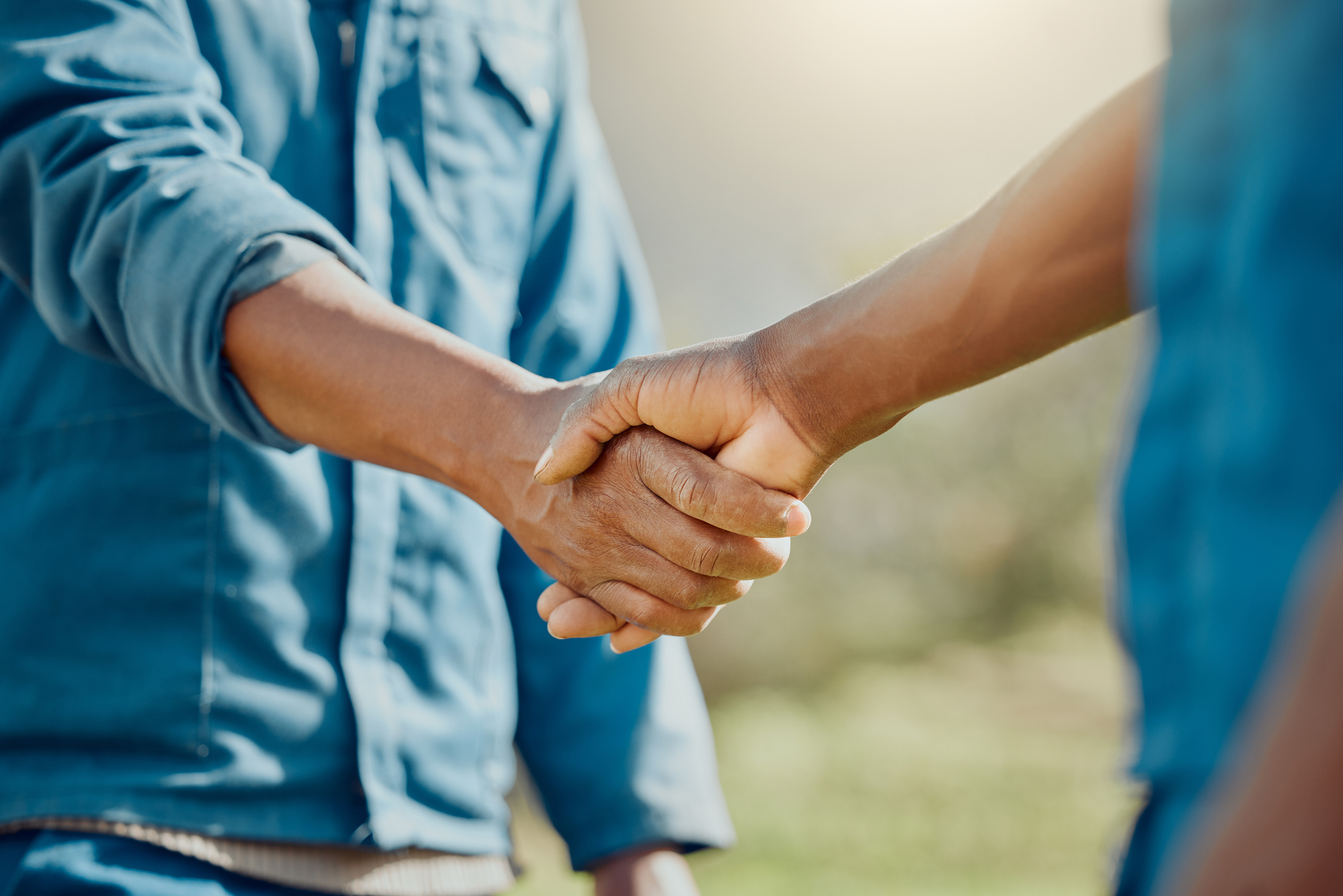 two men in blue working shirts shaking hands with a green field behind