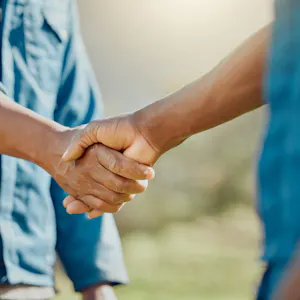two men in blue working shirts shaking hands with a green field behind
