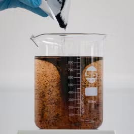 a beaker containing a solution in which a brown powder is being dumped in to test how/if it dissolves