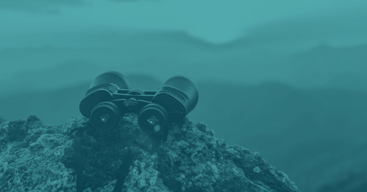 A pair of binoculars set down on a peak looking out over some mountains in the distance. 