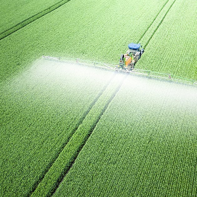 Farm equipment spraying a large, green field.