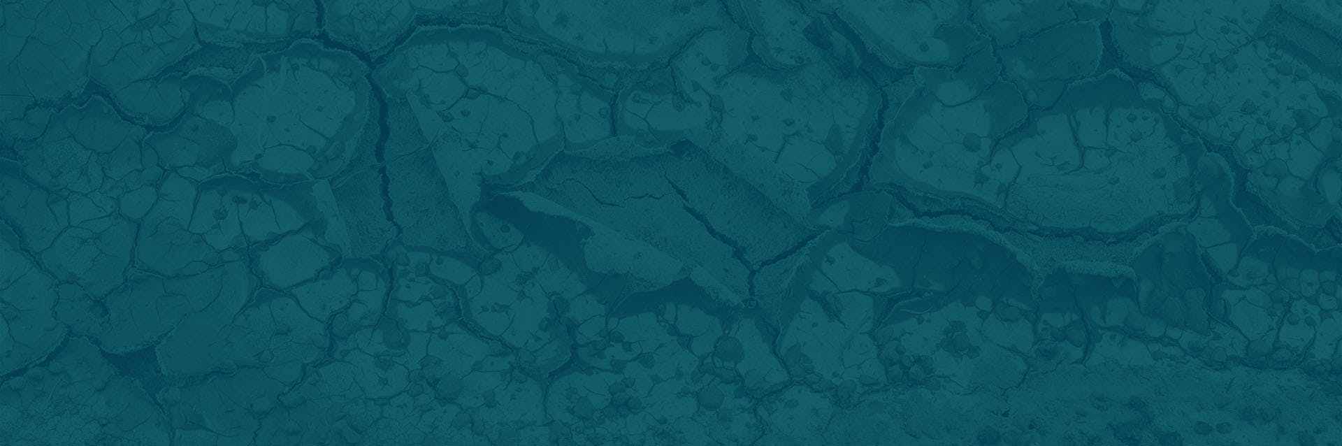 A dirt ground is shown that has been affected by extreme drought. The earth is cracked and dry.