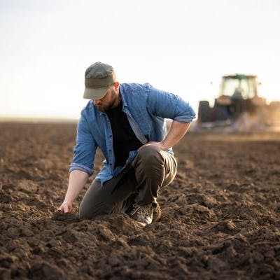 young farmer kneeling in field to examine soil