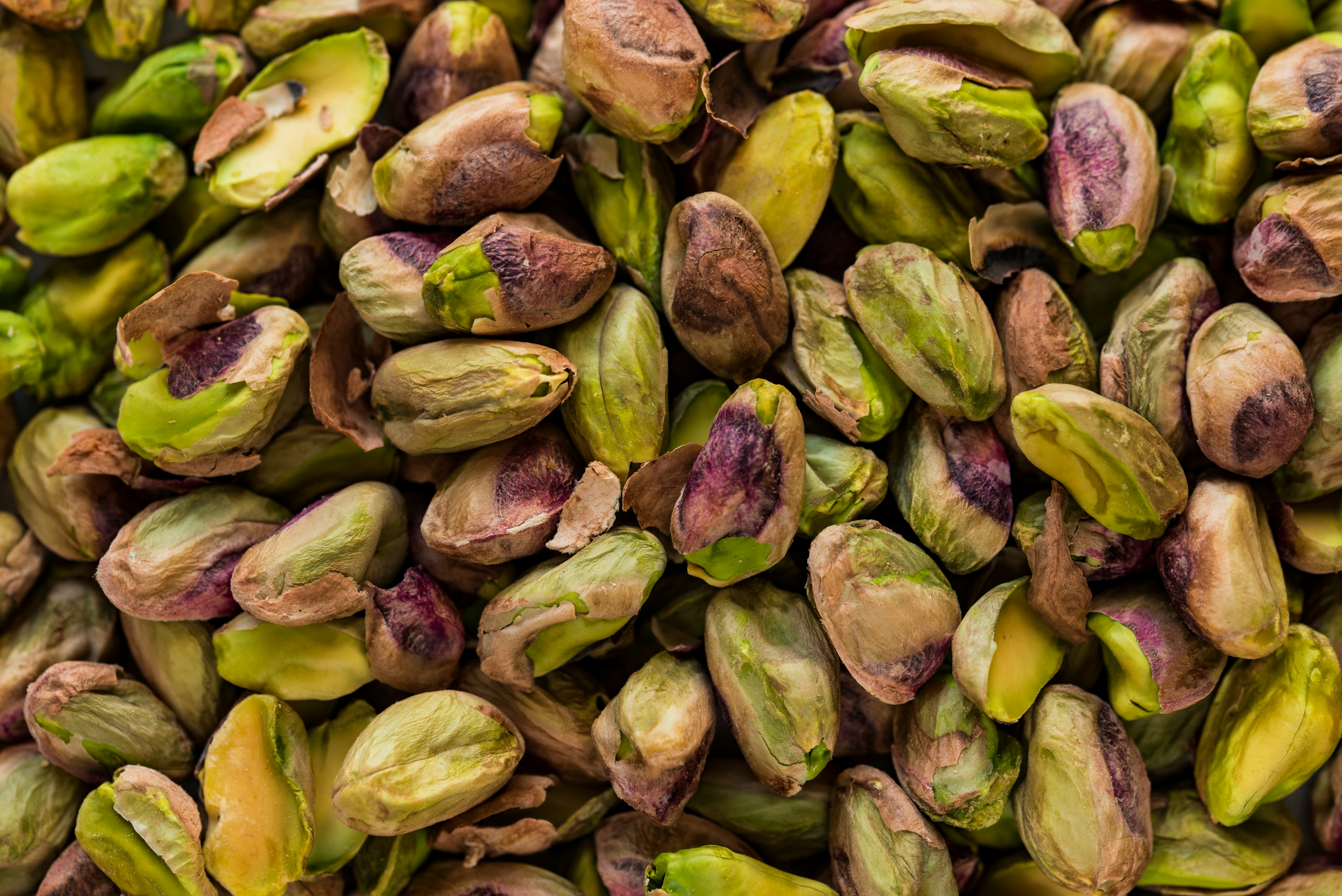 A close up view of mny pistachios out of their shells and piled on top of one another.