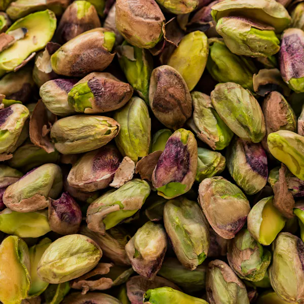 A close up view of mny pistachios out of their shells and piled on top of one another.