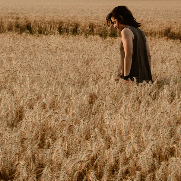 A woman walks through a vast field of tall wheat.