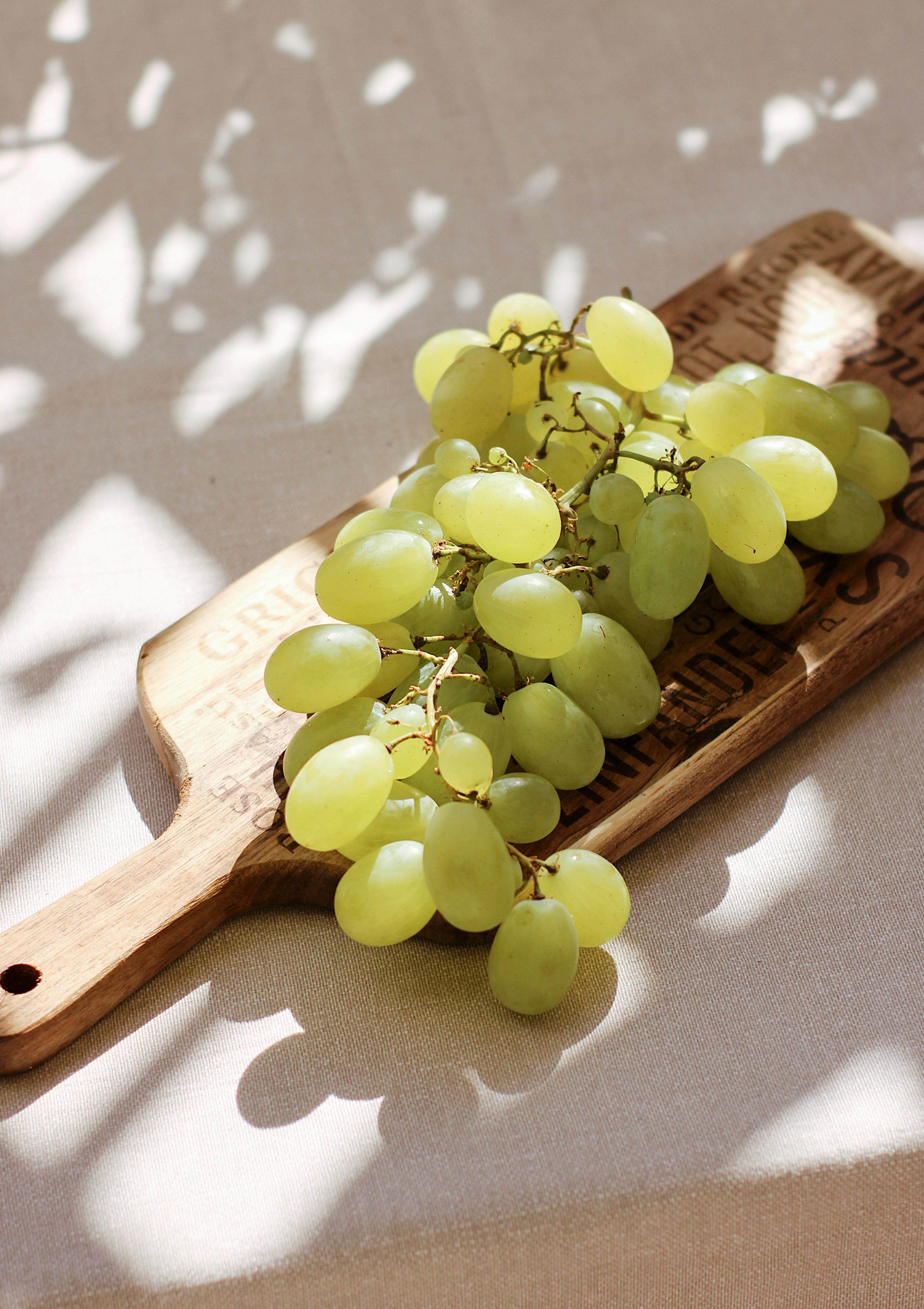 A wooden platter with green grapes sitting on it.