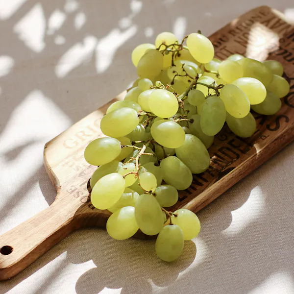 A wooden platter with green grapes sitting on it.