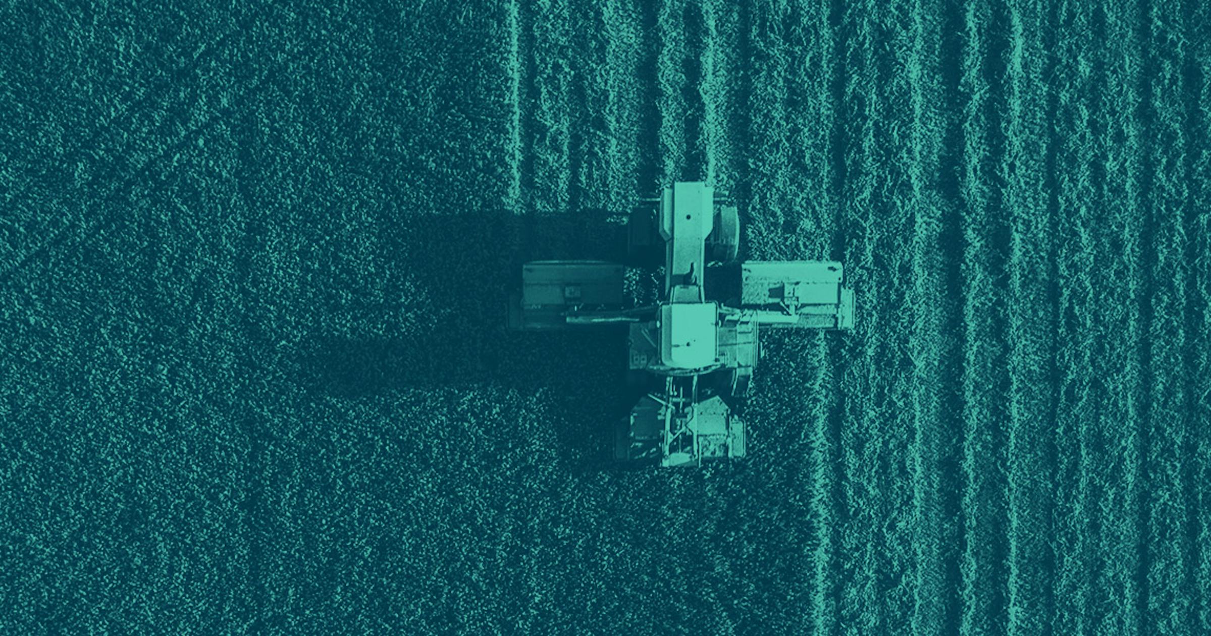 An aerial photo looking down on a tractor in a field, cutting a crop in a neat line.