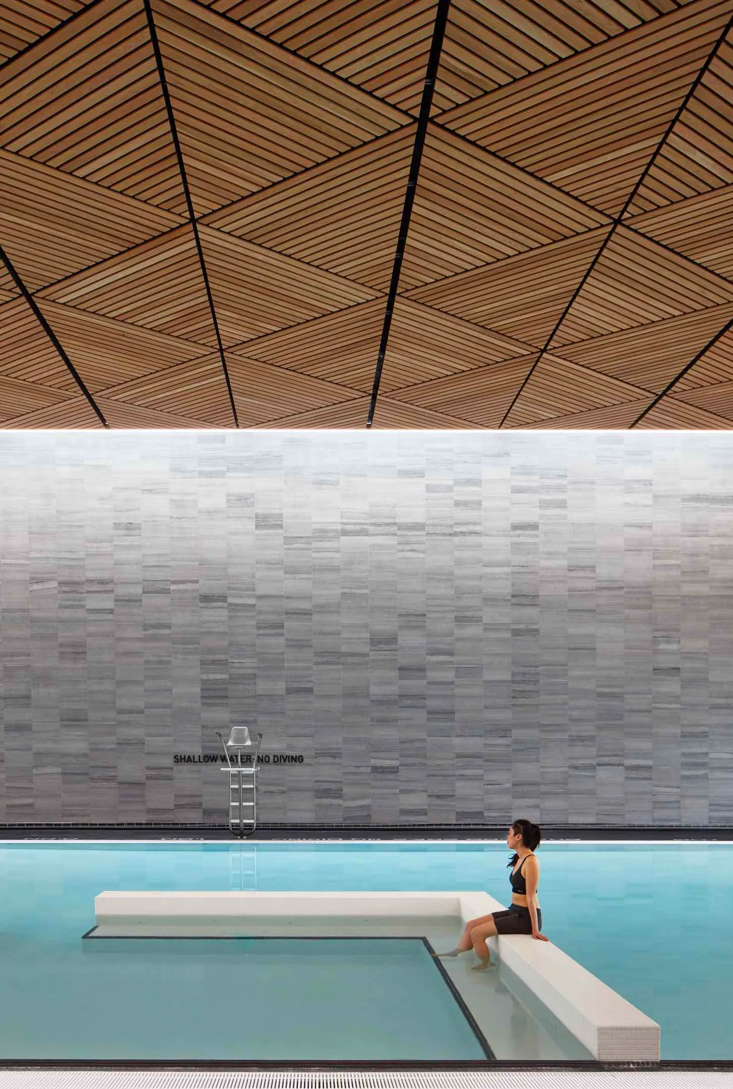 A person seated at the edge of a modern indoor pool with a geometric ...