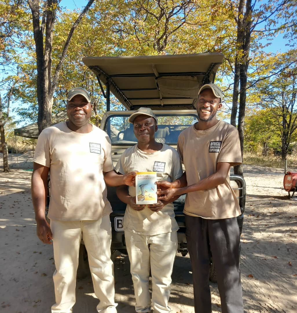 Project staff holding book purchased for them by volunteer on Okavango Wilderness Project - Charles Pfeifer