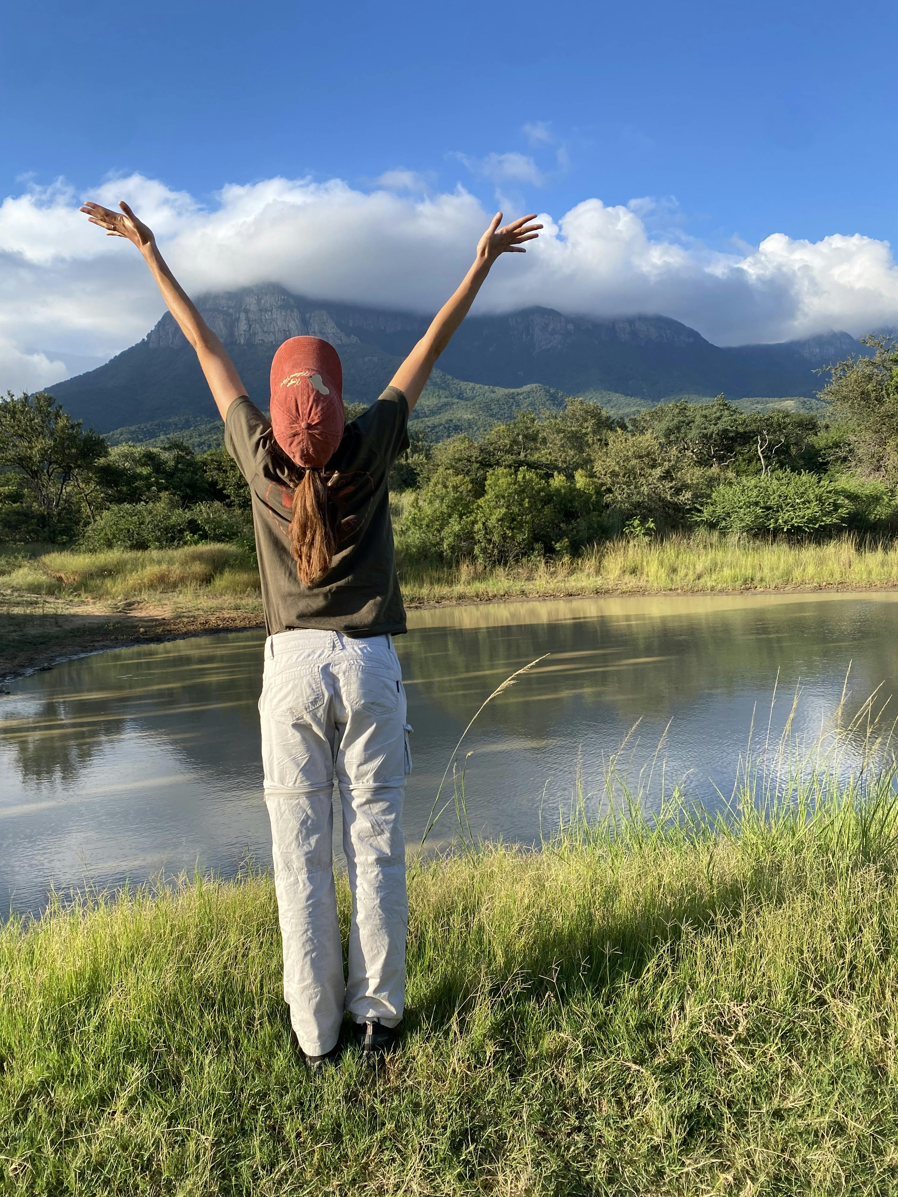 A girl cheers in front of a beautiful landscape at Moholoholo
