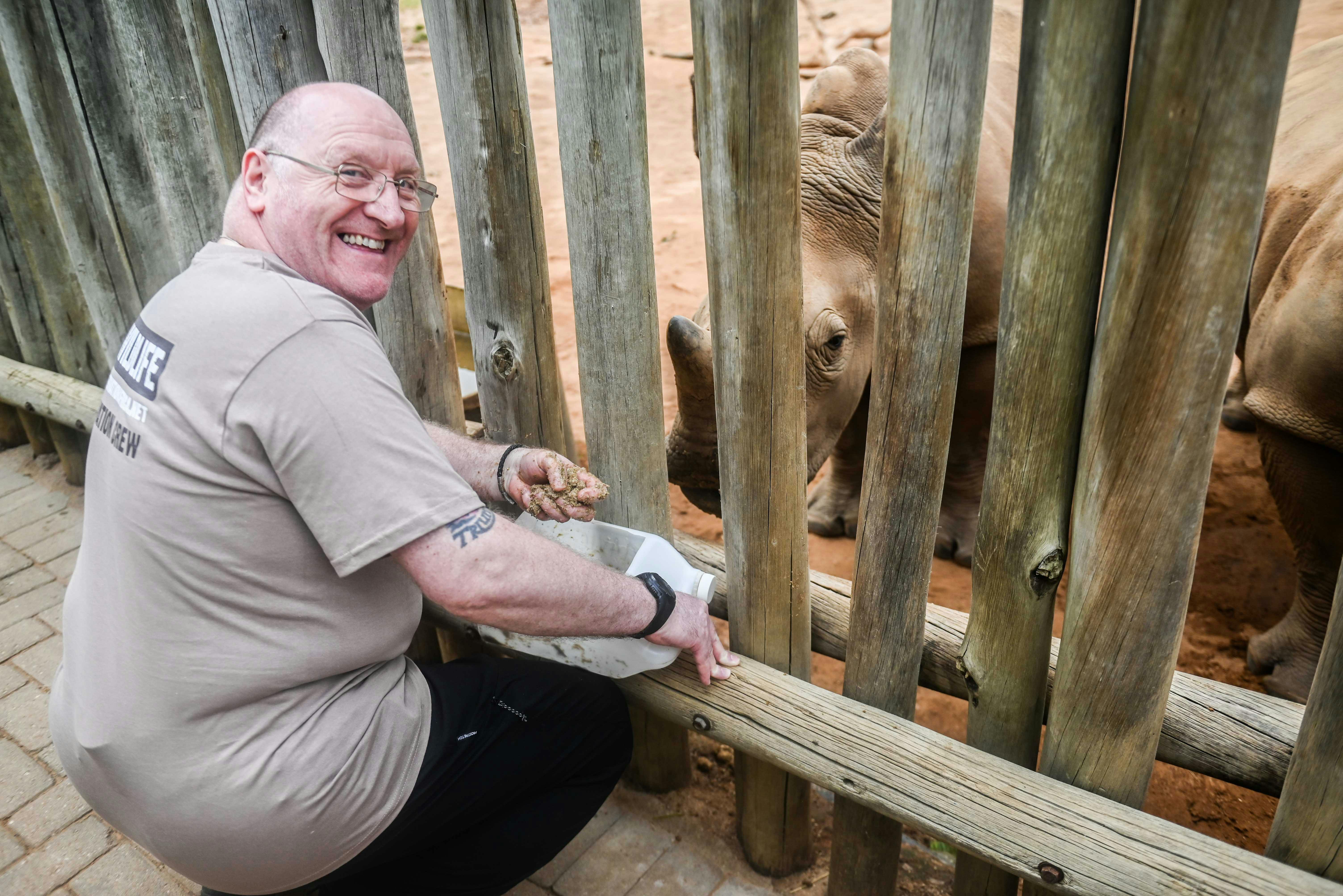 Male volunteer smiling at the camera as he feed a rhino, Care for Wild Africa