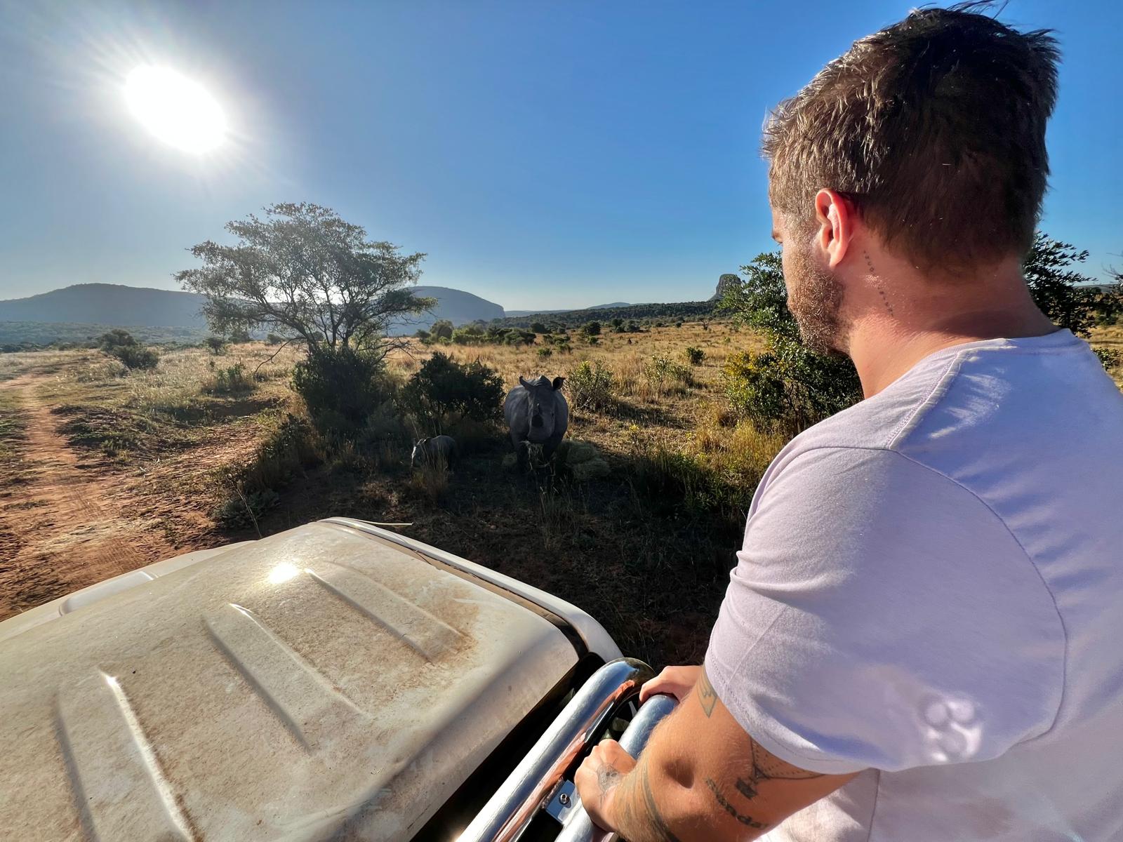 Sam Duggan: male volunteer posing baby rhino landscape