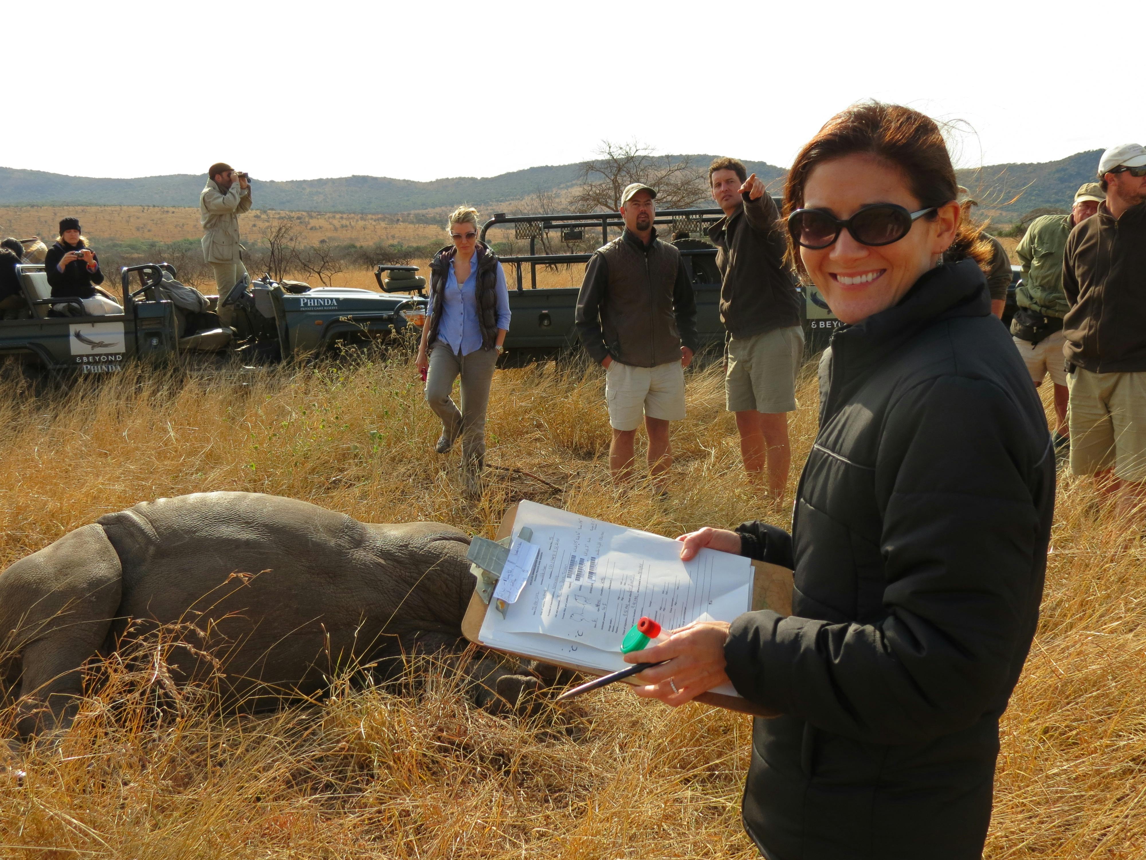 ACE volunteer smiling at the camera while monitoring a sedated rhino