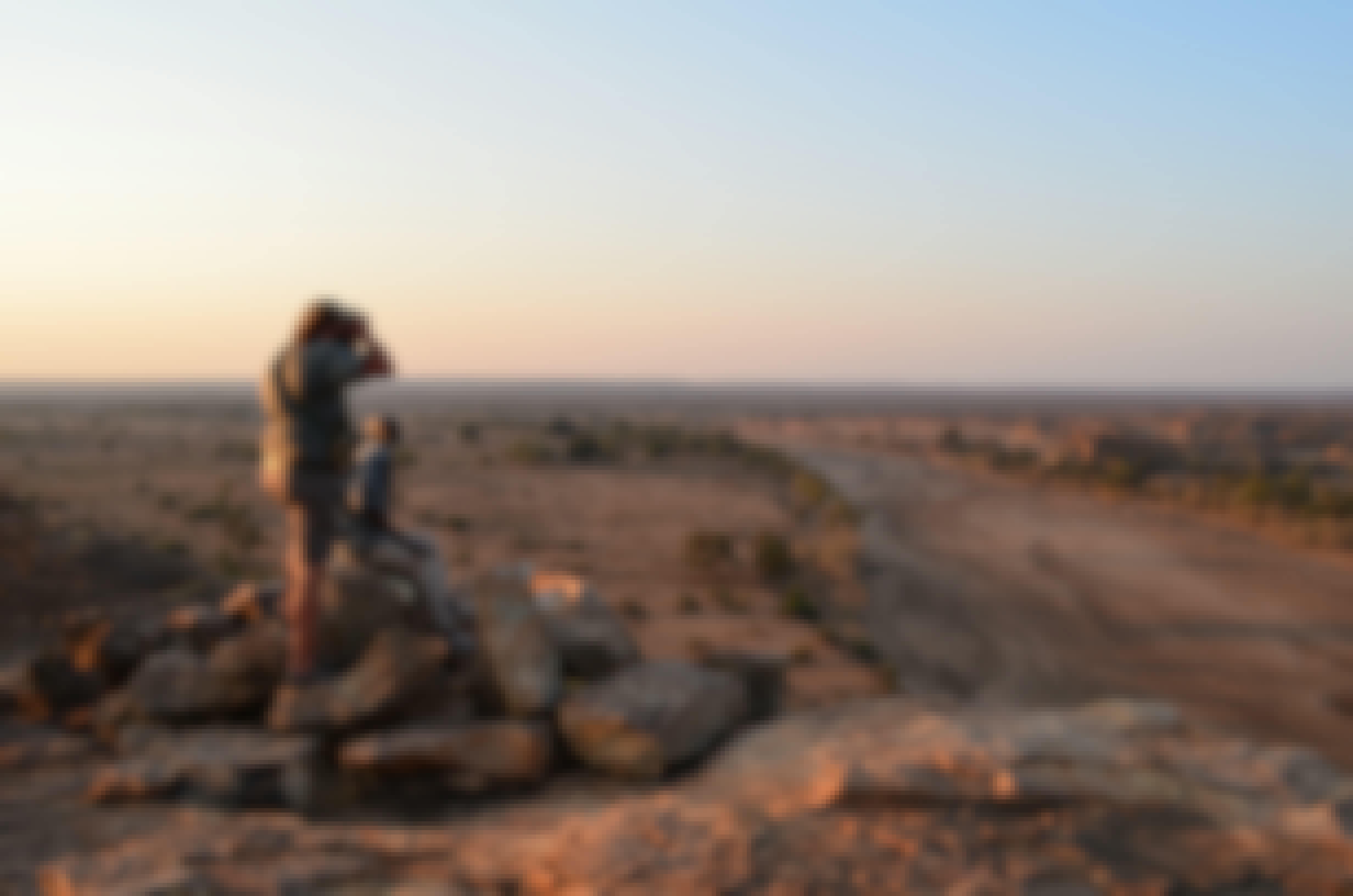 2 men surveying the landscape onto of a pile of rocks, high up in the African bush