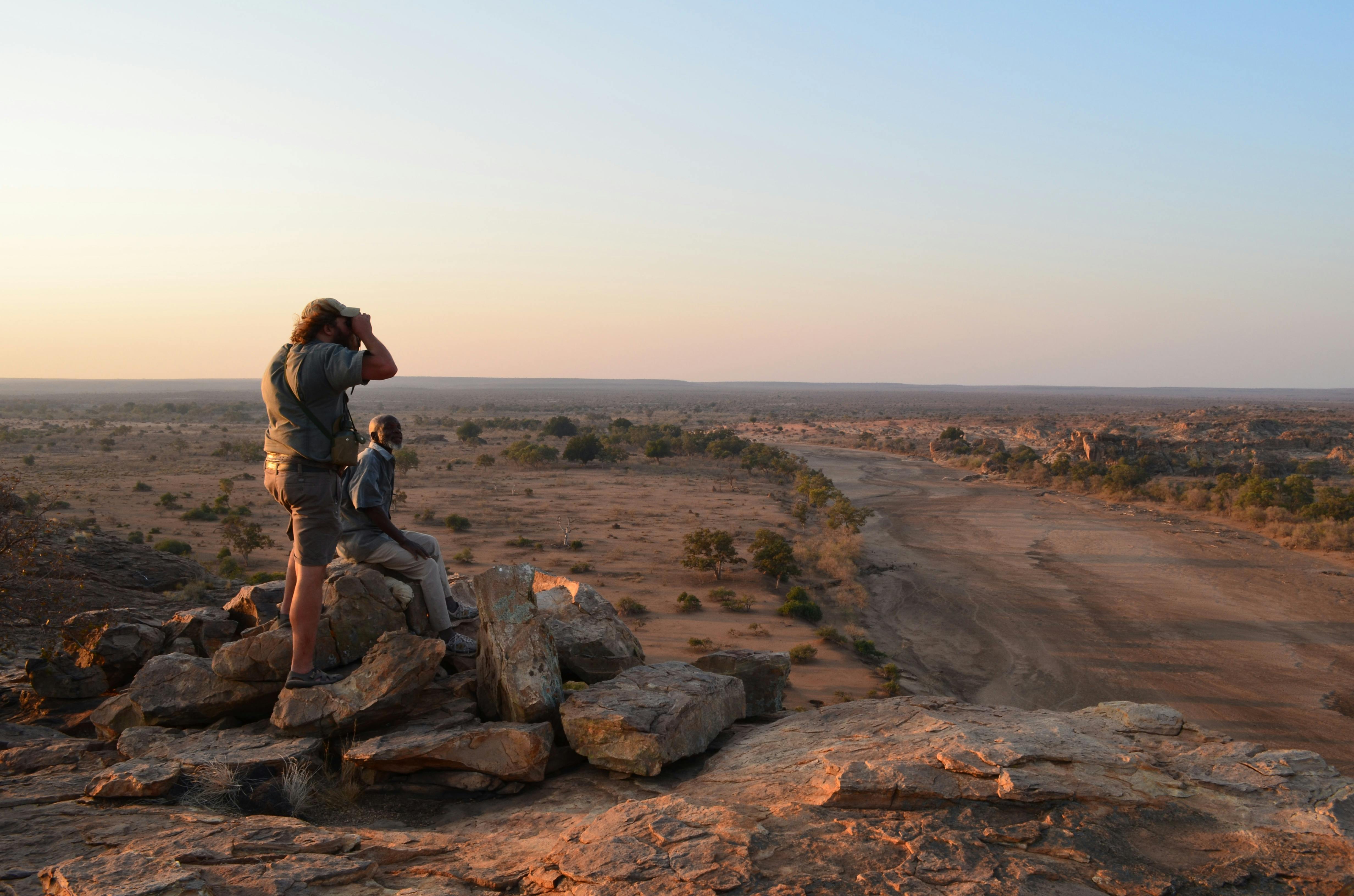2 men surveying the landscape onto of a pile of rocks, high up in the African bush