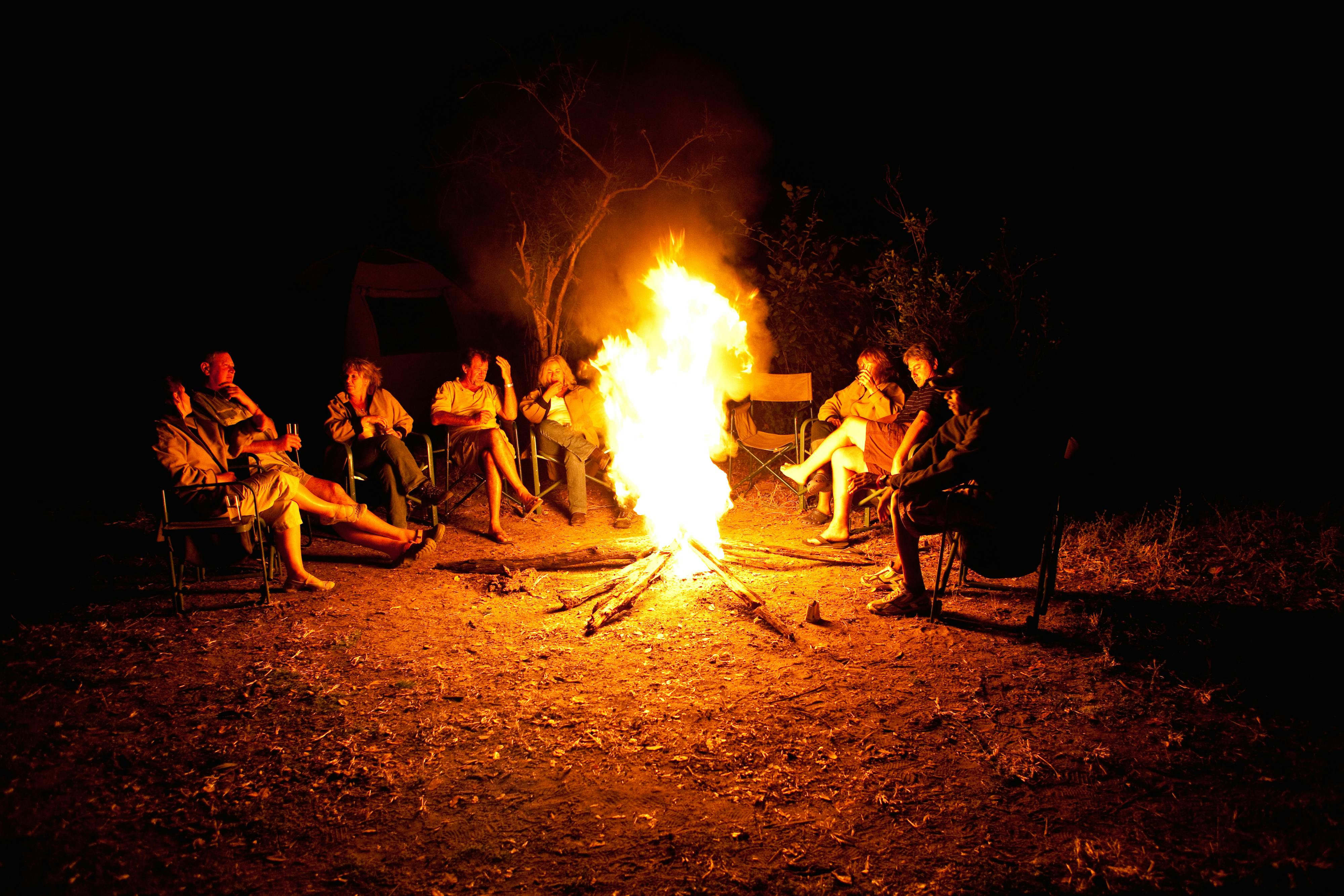 A group of ACE volunteers and staff gathered around a camp fire at night time in the African bush