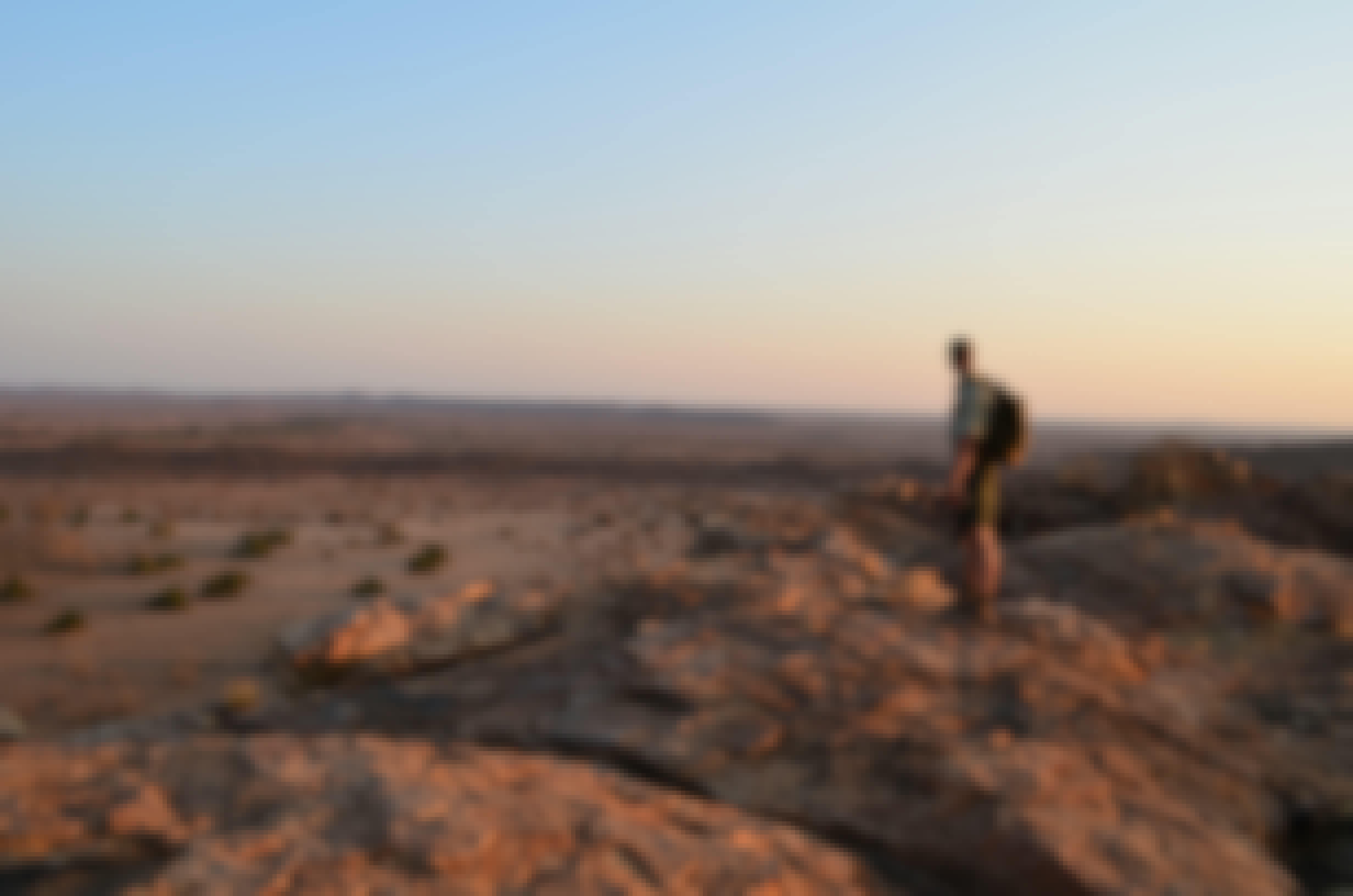 An ACE volunteer standing on a rocky outcrop in the African bush surveying the landscape at sunset