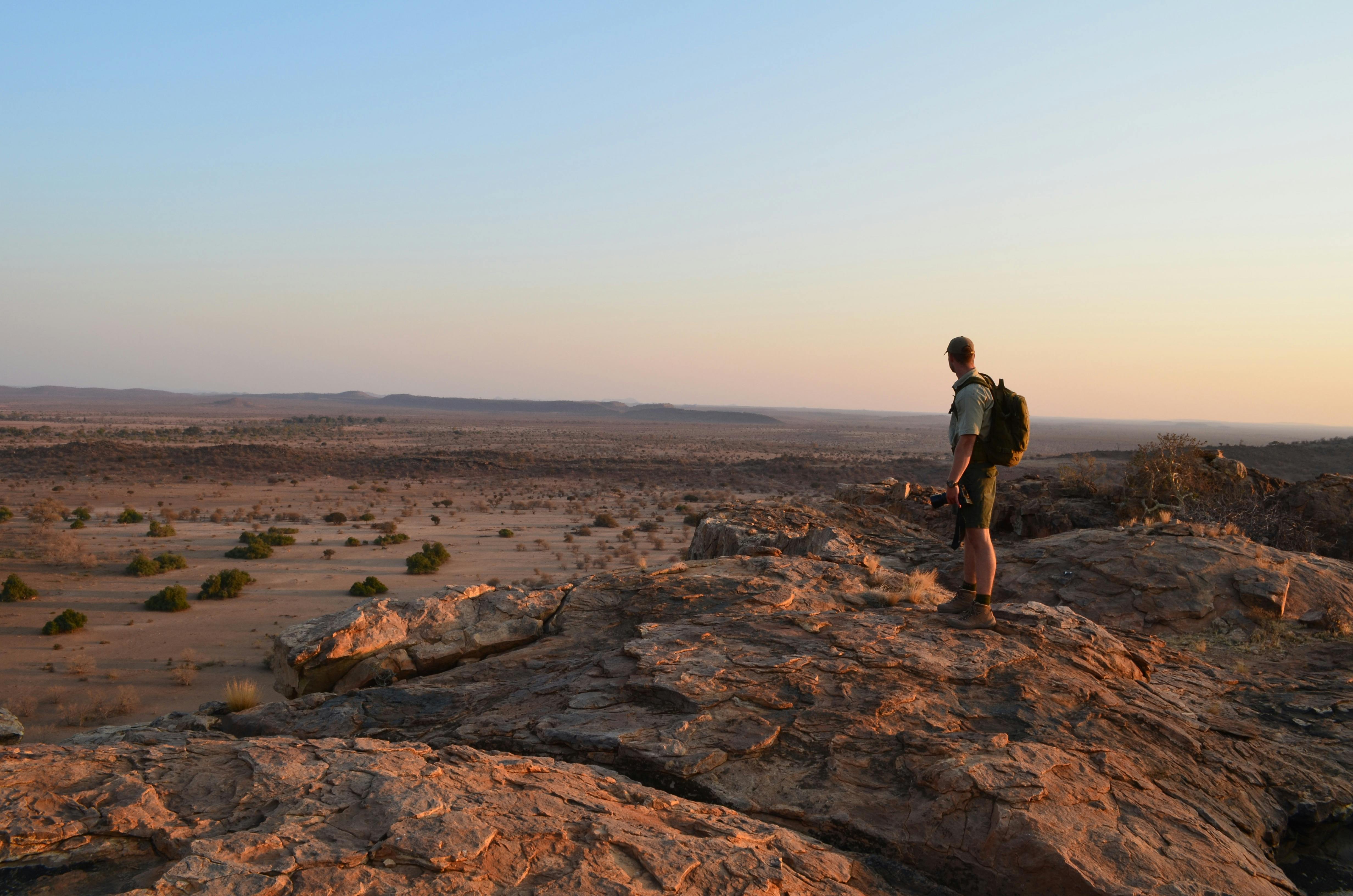 An ACE volunteer standing on a rocky outcrop in the African bush surveying the landscape at sunset