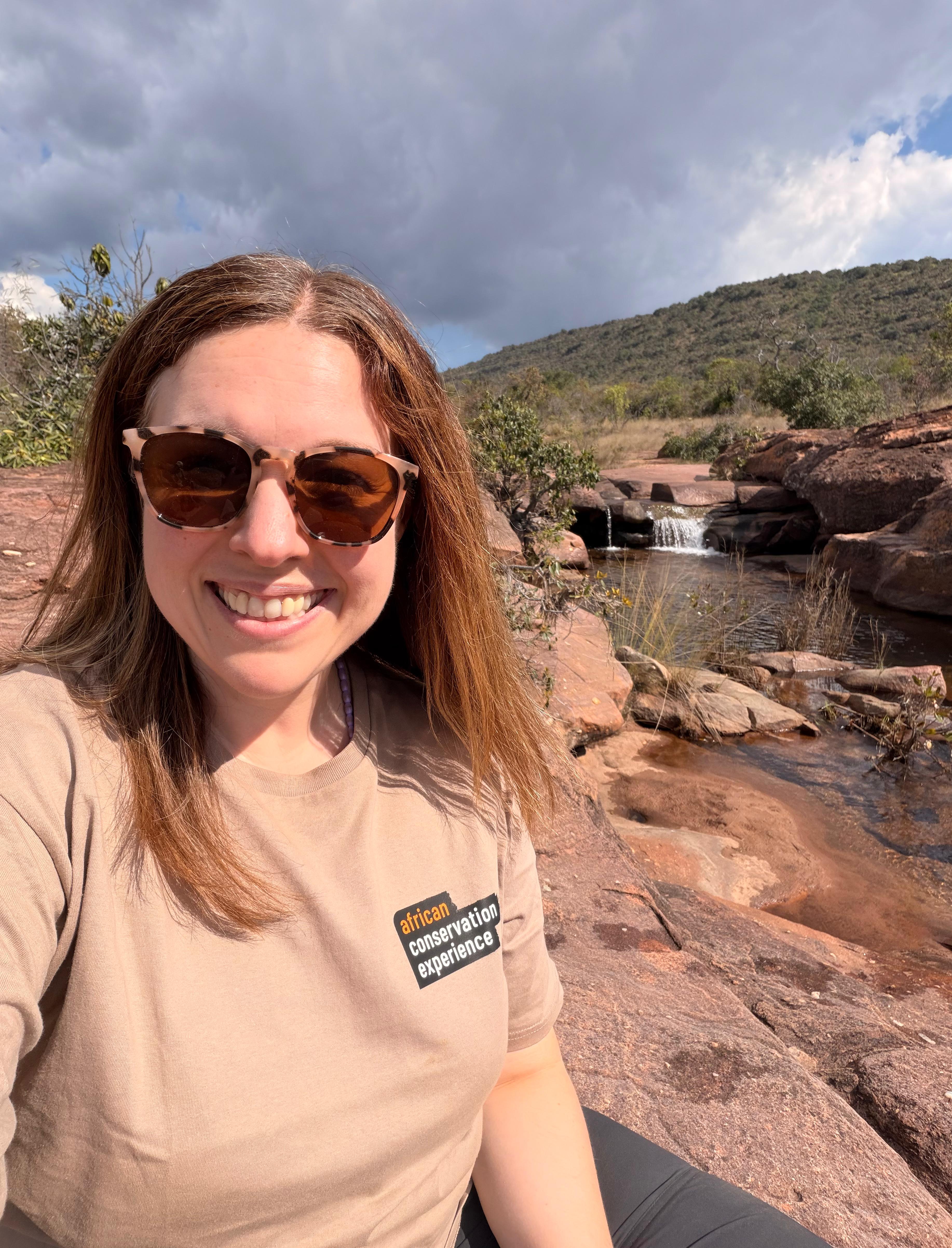 Michelle Revai - Smiling in her ACE t-shirt in front of a waterfall