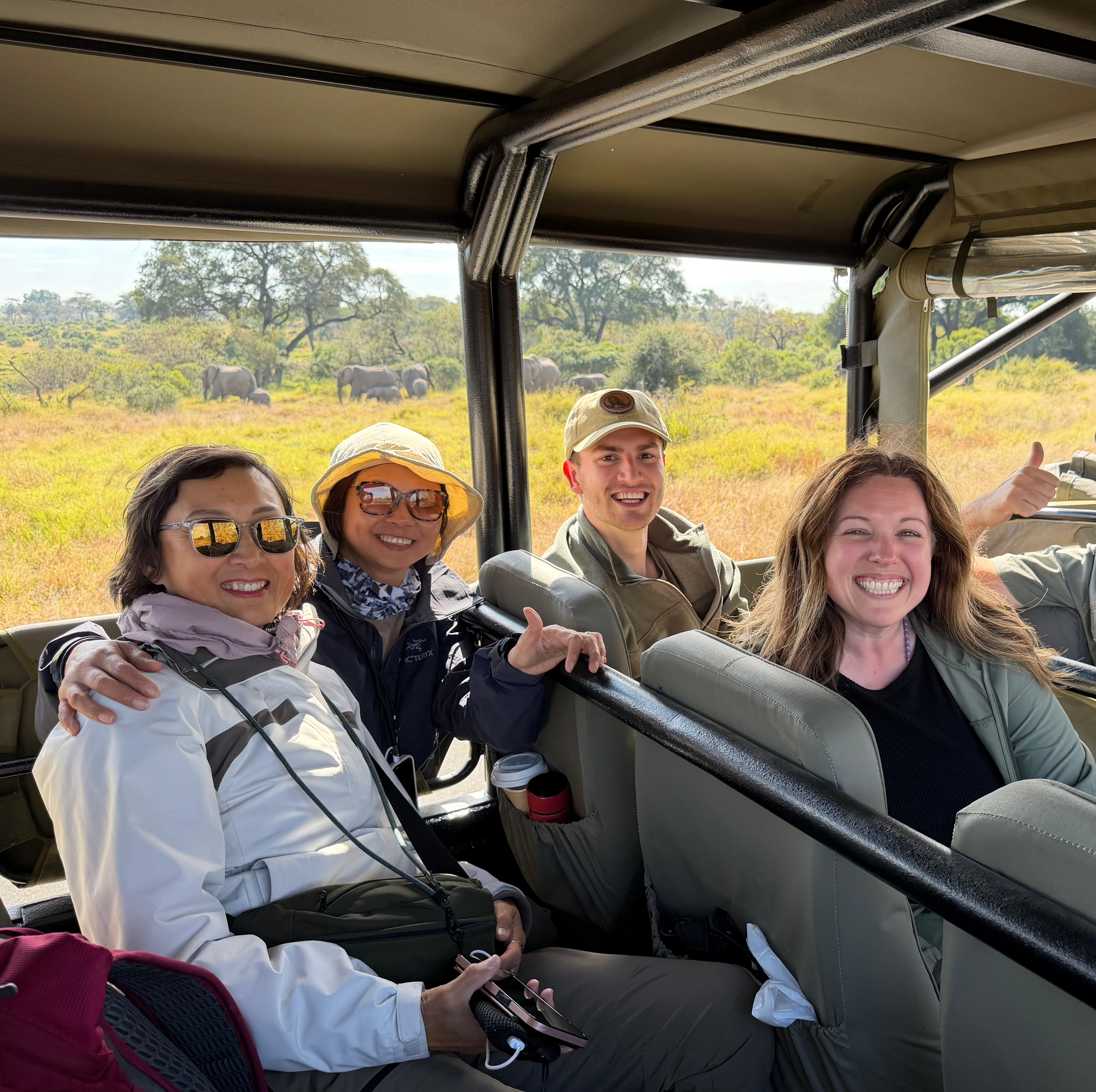 Michelle Revai - Group photo of smiling volunteers on game drive vehicle with elephant herd in the background
