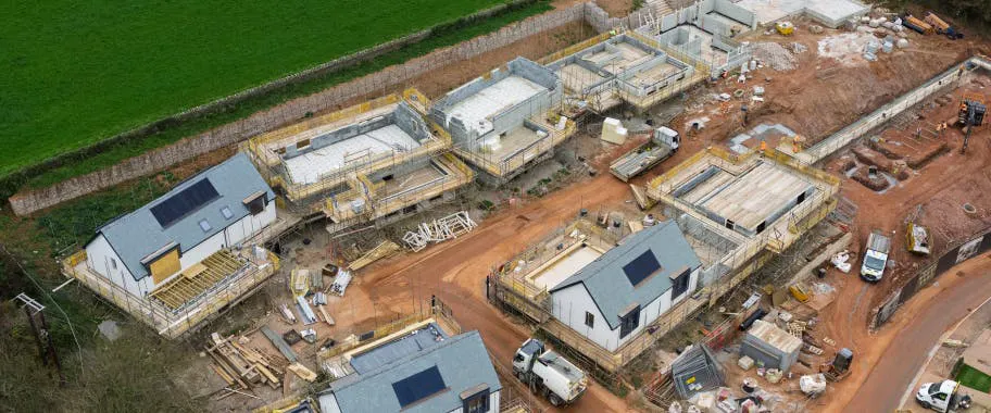 The first row of homes is visibly advanced, while groundworks are underway at the top of the site for the next phase of the build.