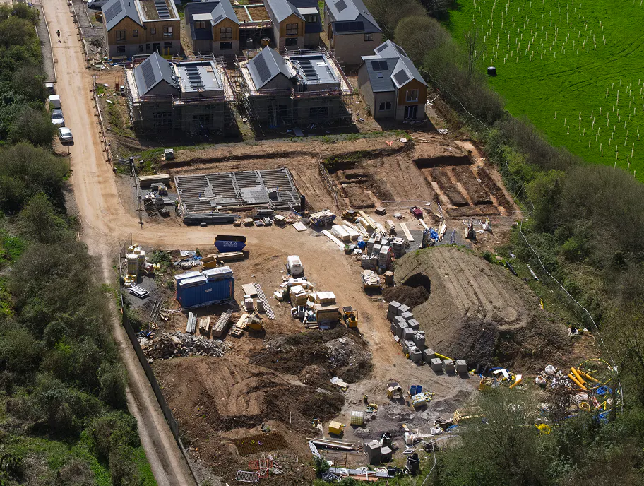 The full arc of Gatcombe Orchard's progress visible in a single frame. Nearly completed homes with solar panels already in place look out over the bustle of the working site below.