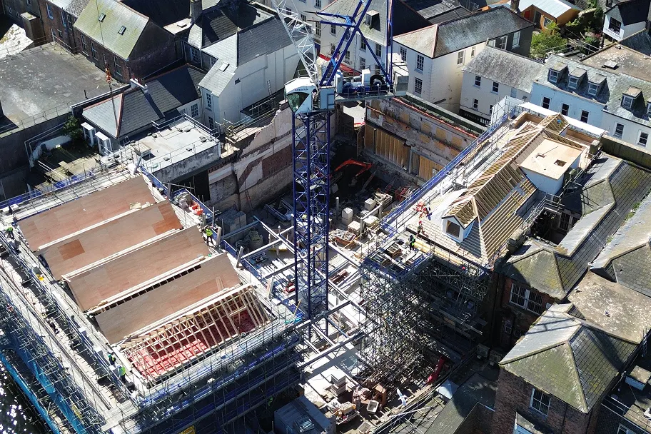 Aerial view of the bank building mid-transformation, with roofing works advanced and the wider site visible beyond.
