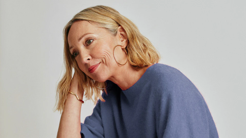 A woman in a blue sweater is seated on a chair, exuding a relaxed and cheerful demeanor.