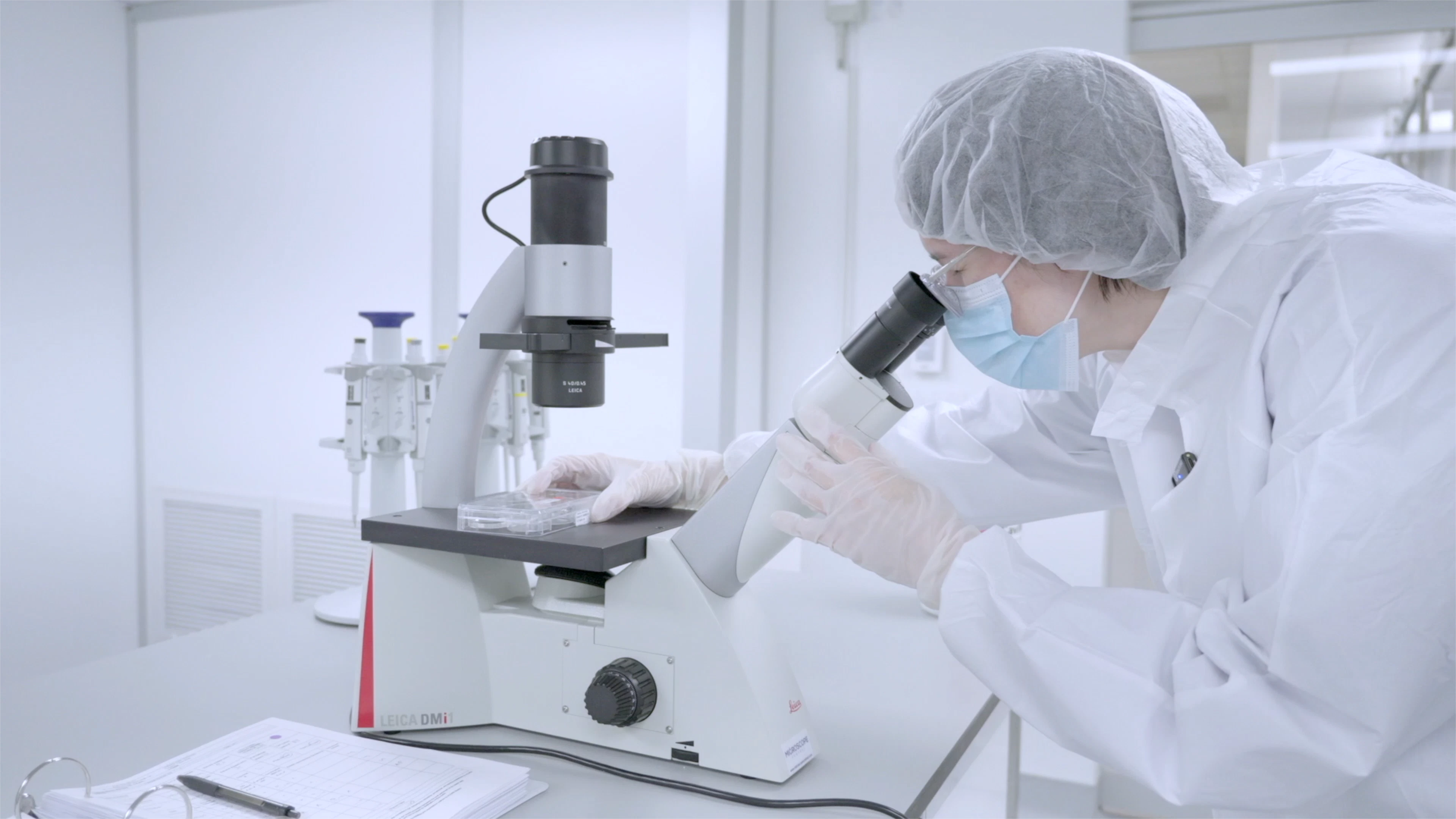 A researcher in a lab coat uses a microscope to analyze stem cell samples in a laboratory setting.