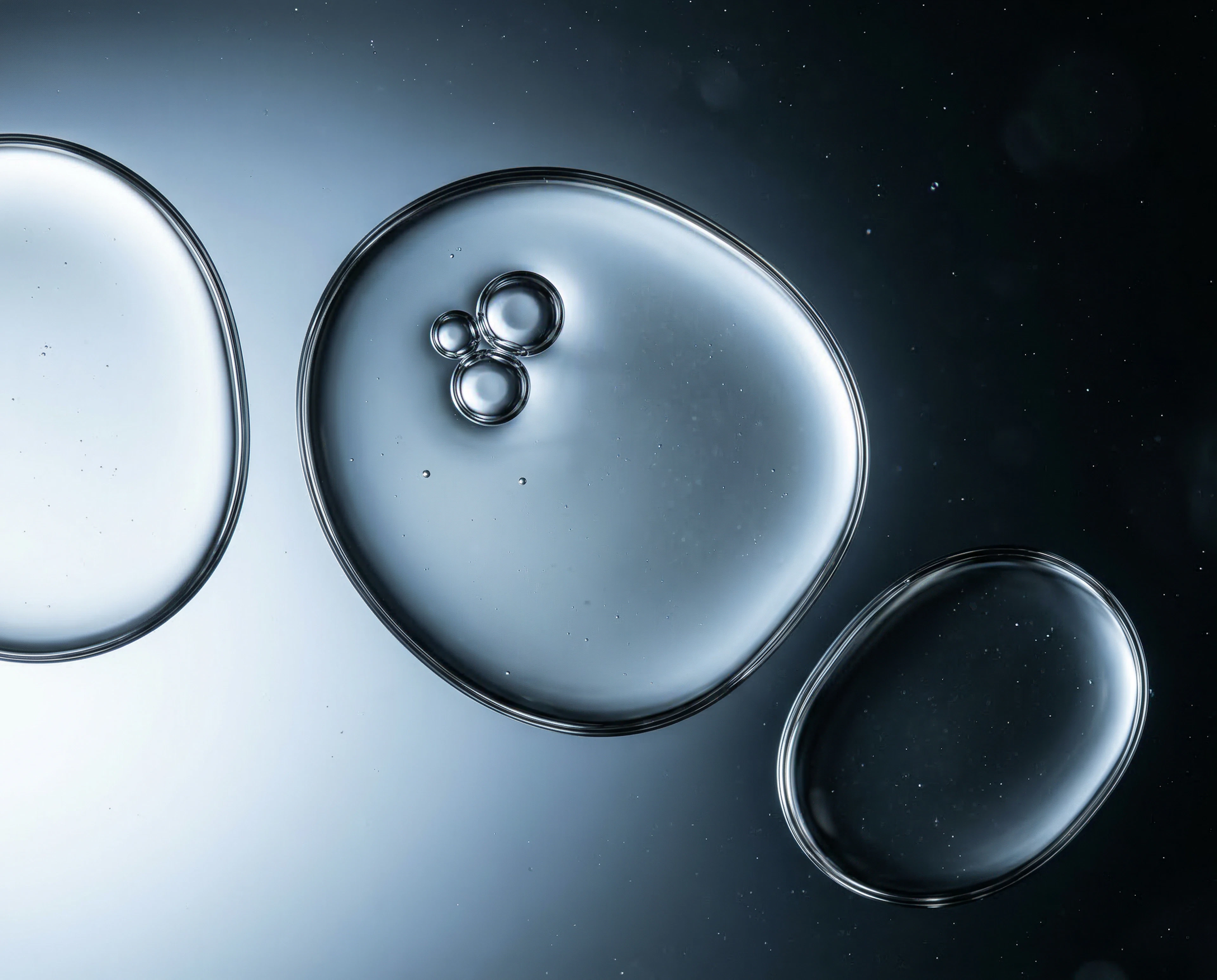 Close-up of serum drops on a black surface, highlighting their reflective surfaces and vibrant hues.