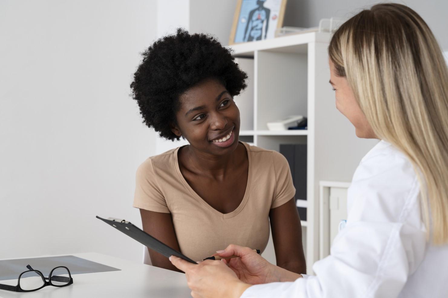 A doctor and a woman are seated at a desk, engaged in a discussion about the woman's health and treatment options.
