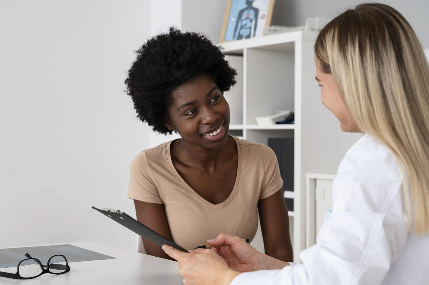 A doctor and a woman are seated at a desk, engaged in a discussion about the woman's health and treatment options.