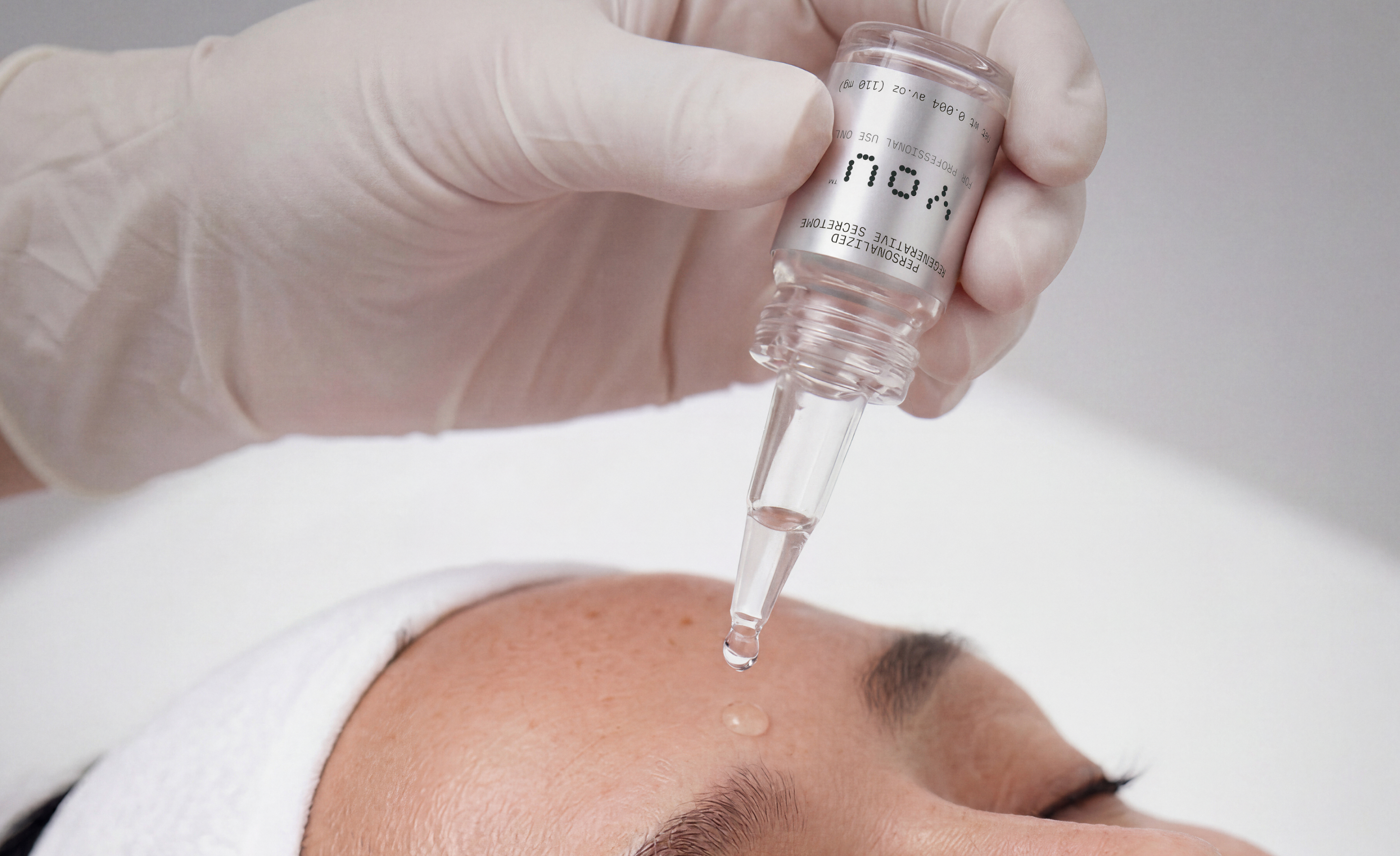 A close-up of a woman using a secretome serum on her face for skin care.
