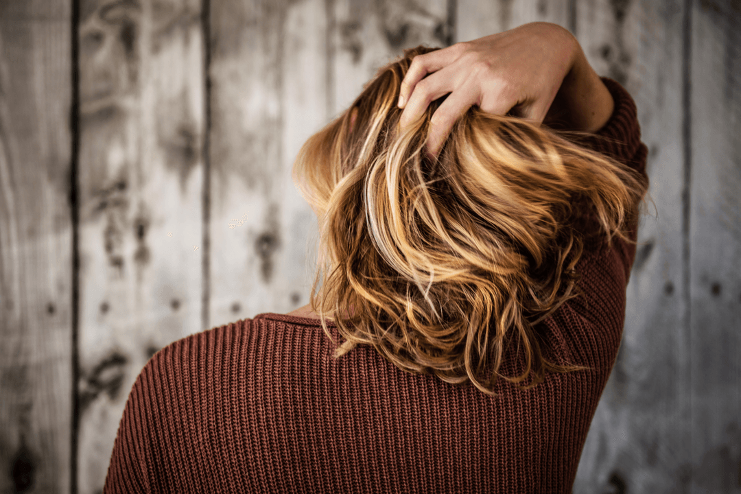 A woman with long hair gently touches her head, appearing contemplative and serene.