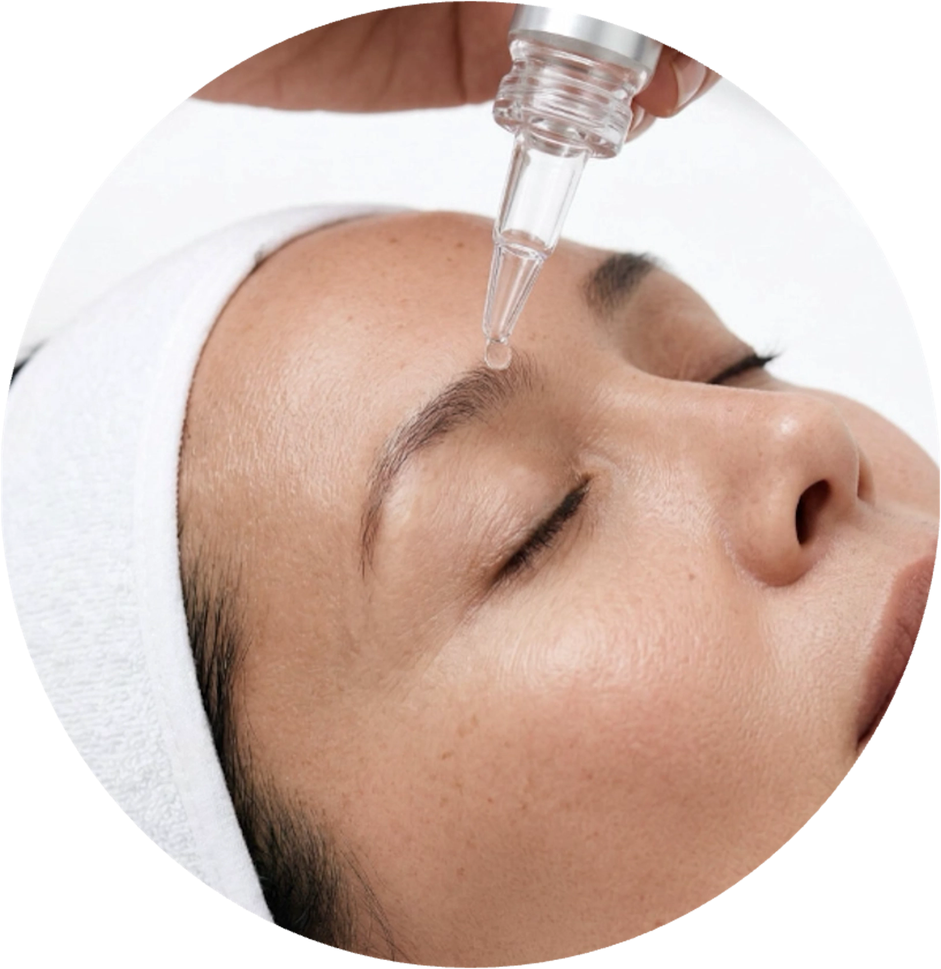 A woman receiving a facial treatment with a dropper applying serum to her forehead.