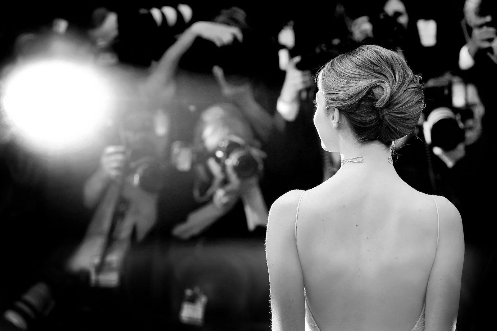 A woman in an elegant backless dress is captured by photographers at a glamorous event.