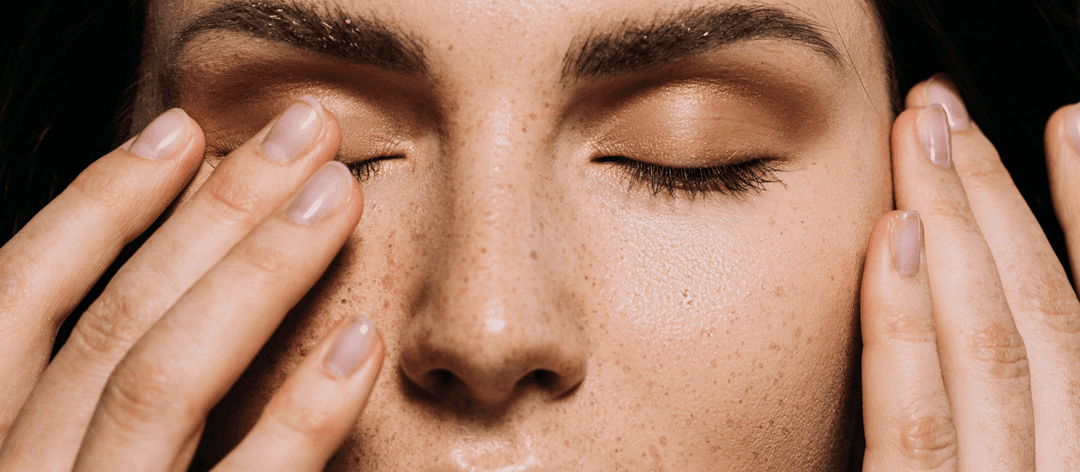 A woman with freckles gently touches her eyes, showcasing a thoughtful expression on her face.