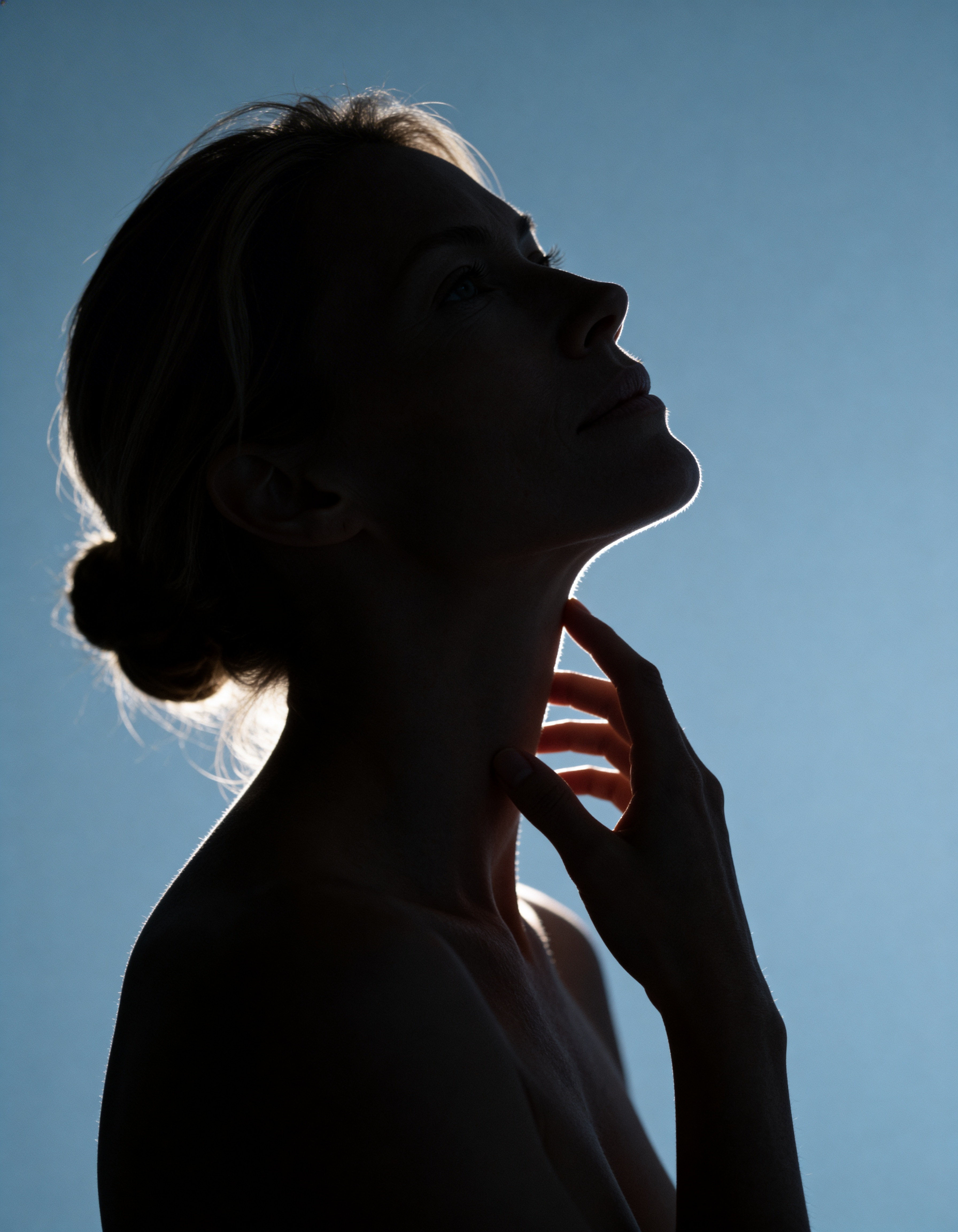A woman’s silhouette with hands resting on her neck, suggesting a moment of reflection or emotional expression.