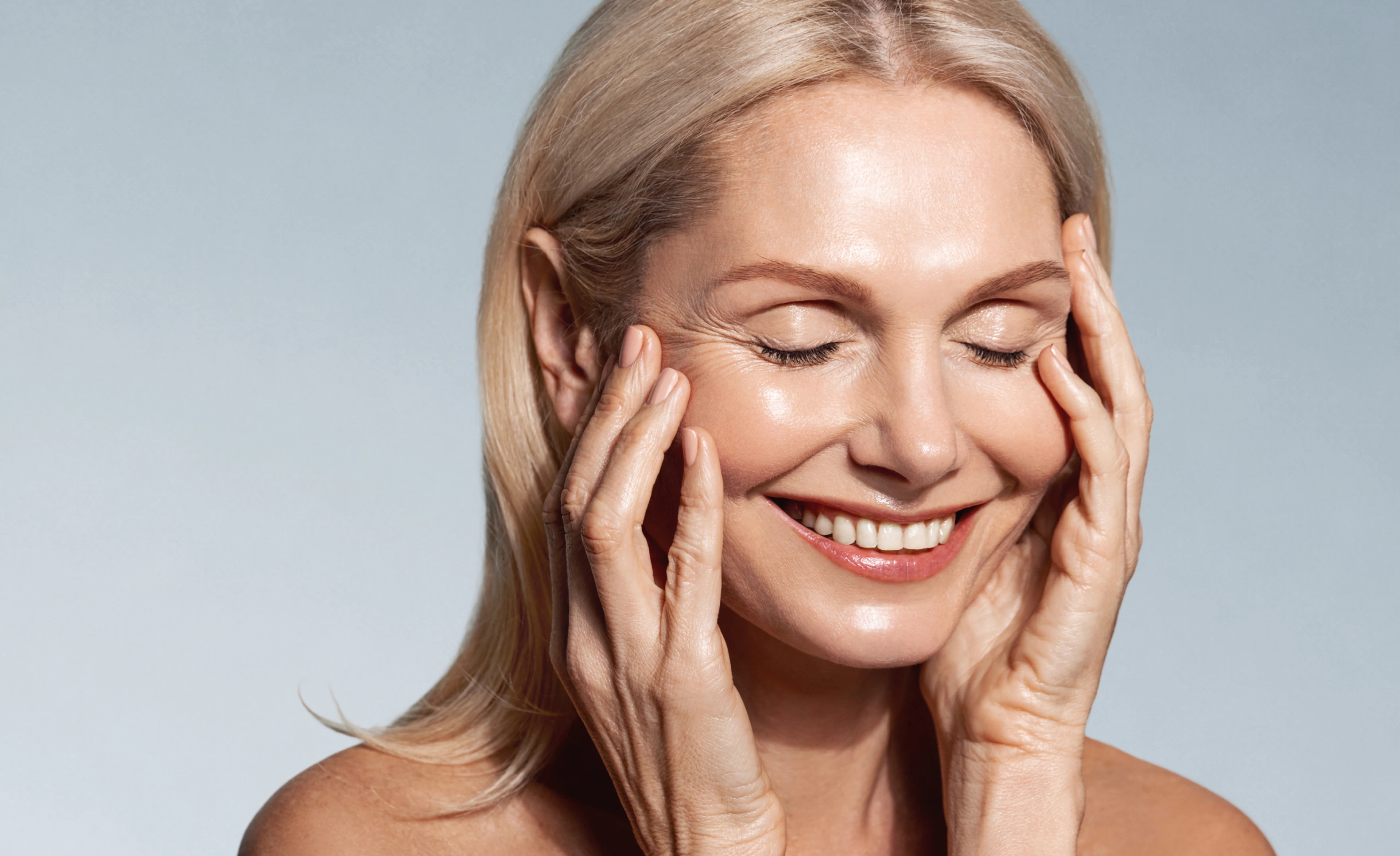 A cheerful woman with a bright smile, her hands placed on her cheeks, expressing delight and positivity.