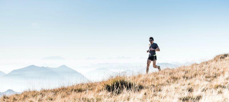 A man running on a mountain top, surrounded by a panoramic view of rugged peaks and clear blue sky.
